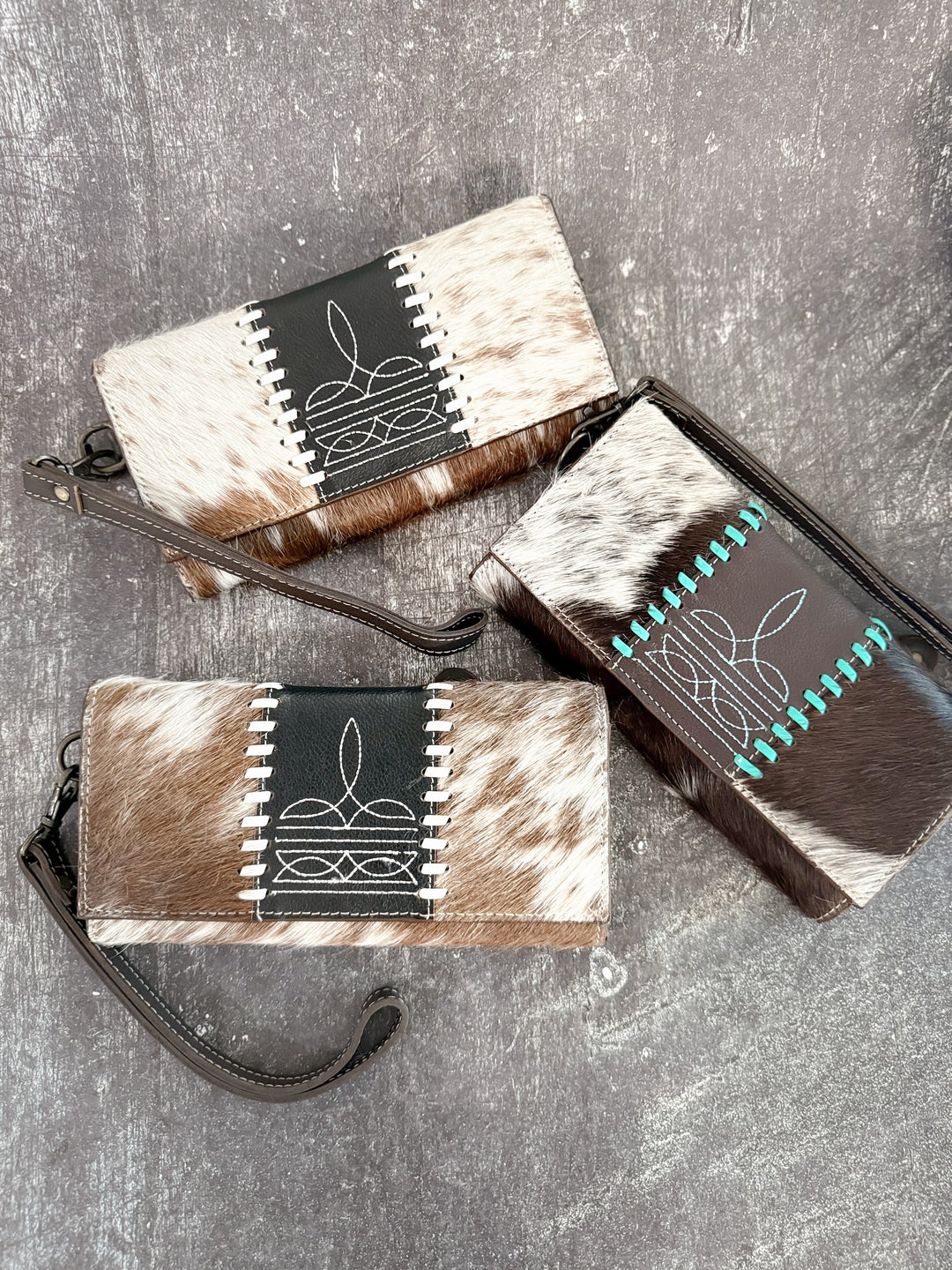 Three cowhide wallets with unique patterns on a gray surface