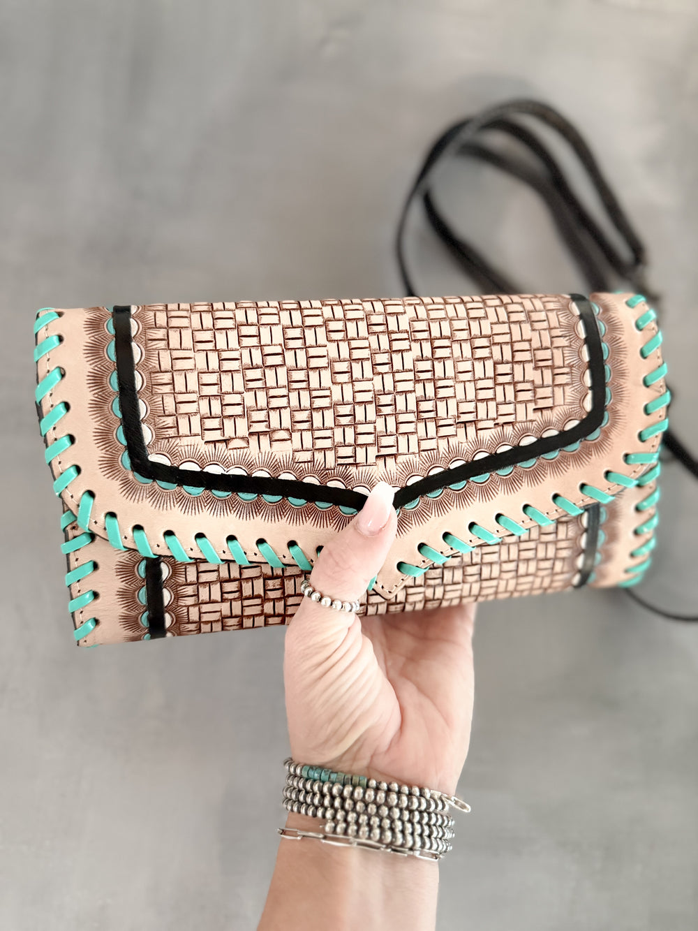 Front view of handmade tooled leather clutch with basketweave design and turquoise whipstitch edges