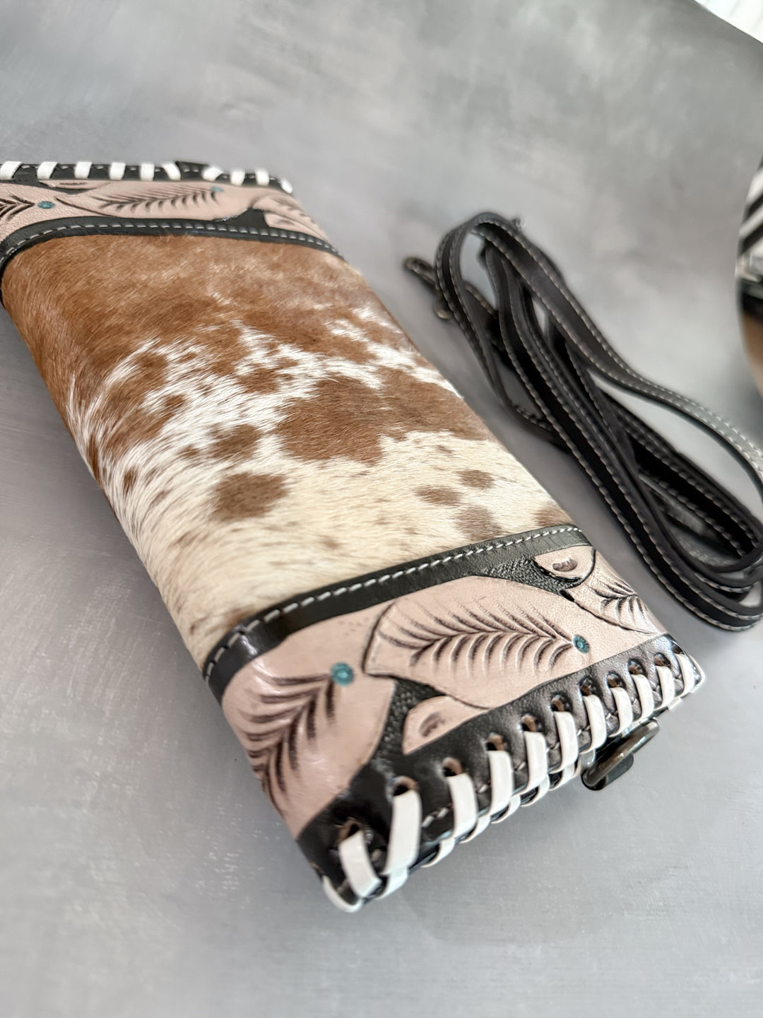 Back view of cowhide clutch with tooled leather feather accents and whipstitch edging