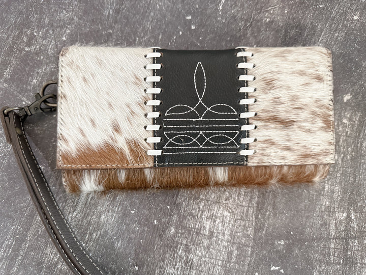 Women’s western wallet with cowhide and boot stitch design leather and black strap on a textured surface