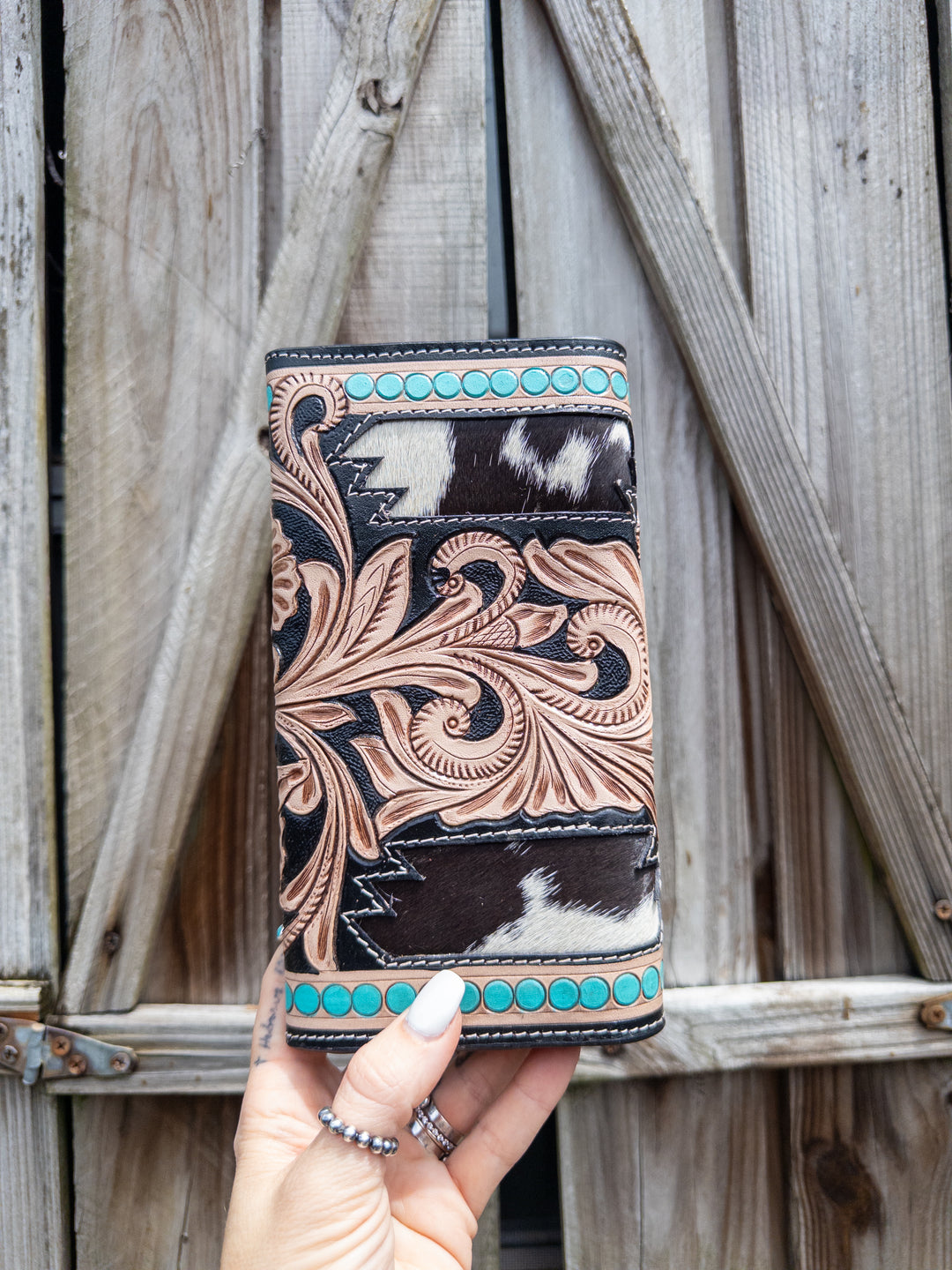 Cowhide and tooled leather wallet with turquoise stud border, floral tooling, and natural hide pattern.