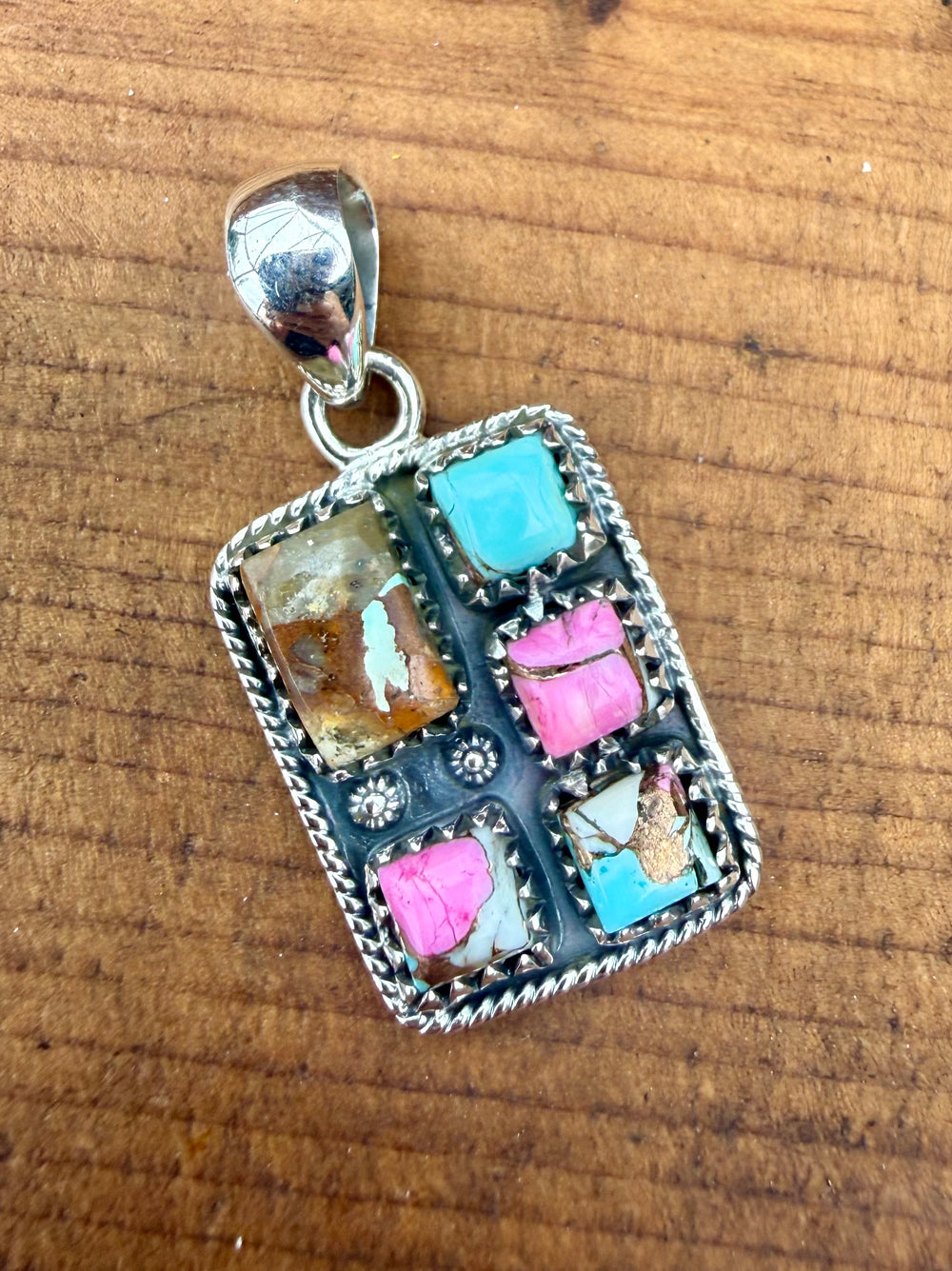 Sterling silver Mine #8 turquoise and pink composite southwestern pendant with stamped detailing and bale on wood background