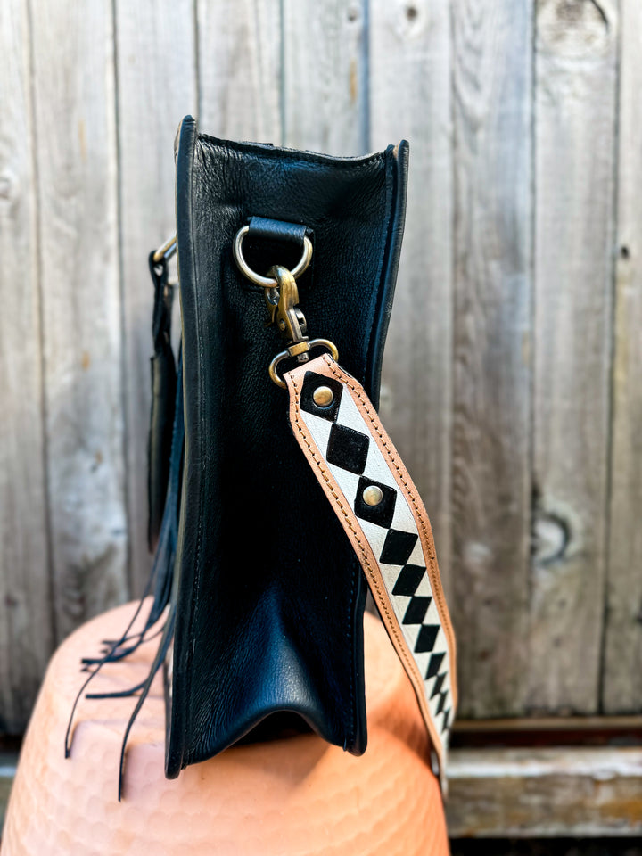 Black leather with tooled leather checkered side view of concealed carry cowhide tote with a tooled checkered strap against a wooden background