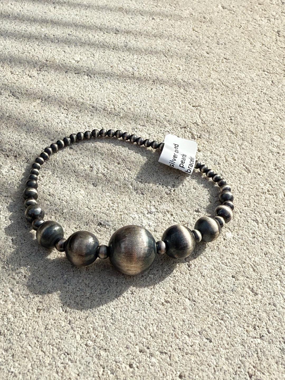 Graduated sterling silver desert pearl stretch bracelet with oxidized finish on flat lay