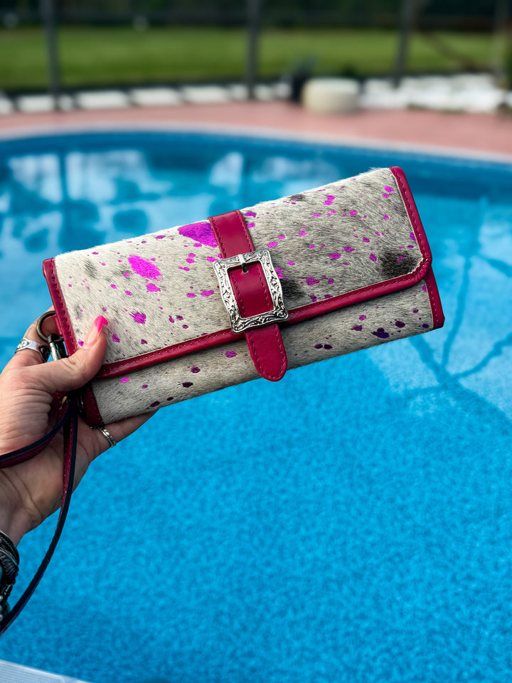 Hand holding a genuine cowhide wallet with pink leather accents and silver buckle by a pool