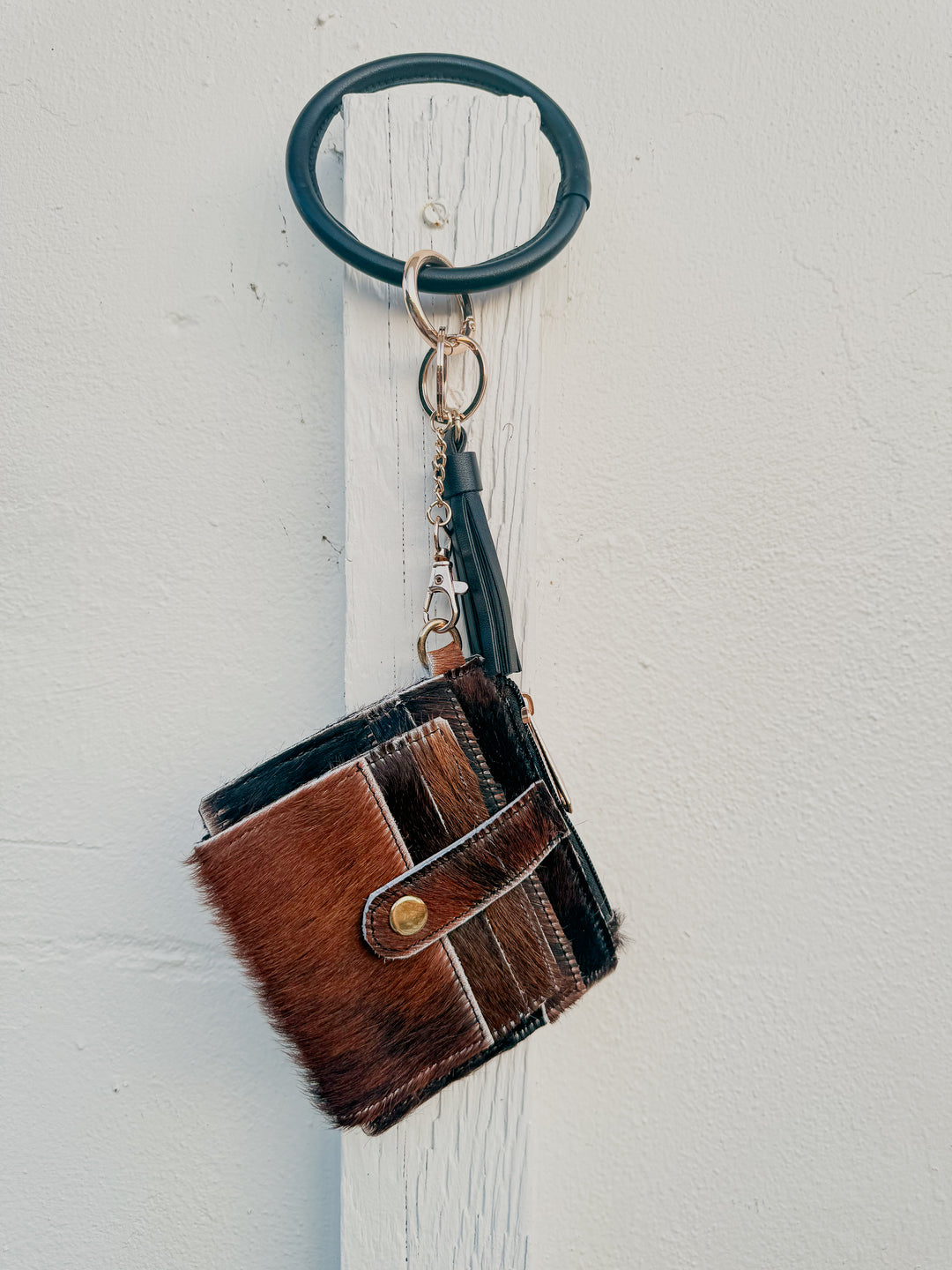 Dark cowhide wristlet wallet hanging from black bangle keyring with leather tassel.