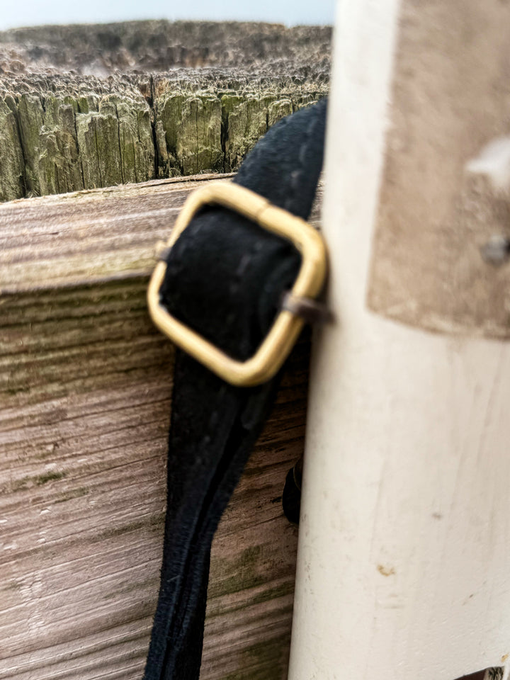 Close-up of adjustable suede strap with brass buckle hardware on crossbody bag