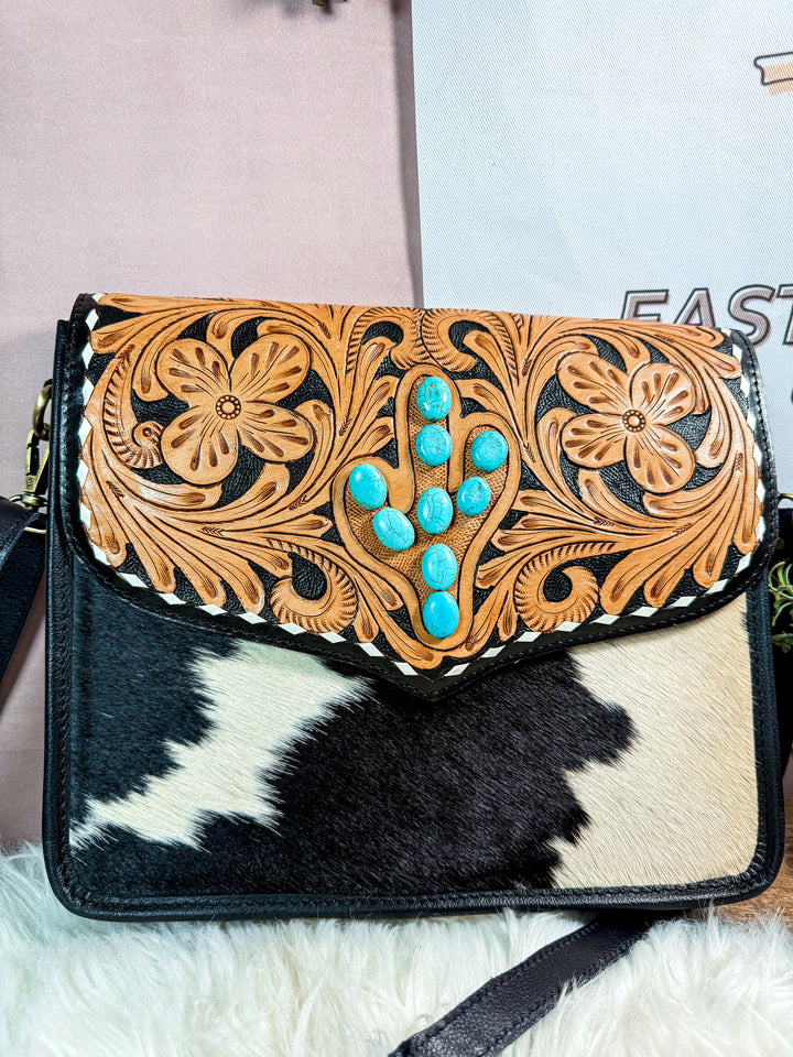 Cowhide leather handbag with floral tooled design and turquoise stones on a white background