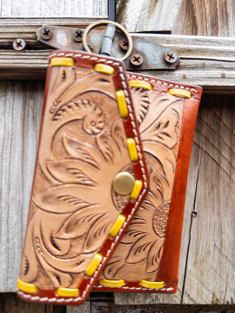 Tooled leather keychain wallet with yellow whipstitch detail and snap closure, front view.