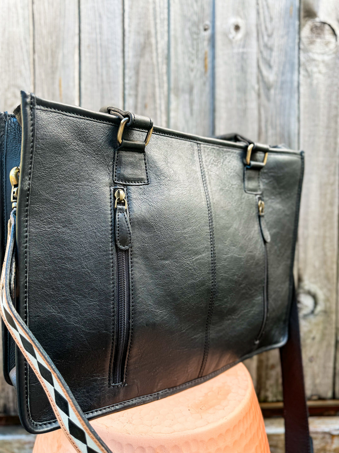 Black leather cowhide and tooled checkered handbag tote with with gold hardware and double zipper concealed carry pocket on a wooden surface