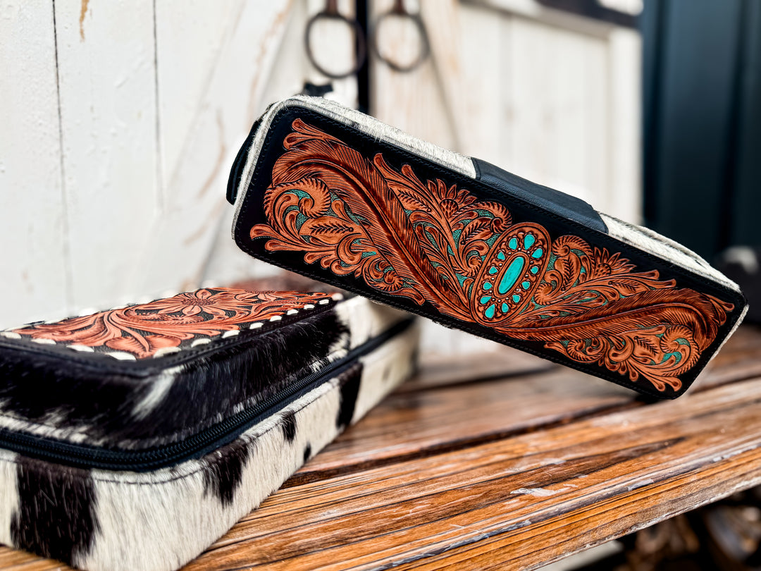 Tooled leather western hair tool travel cases displayed on rustic wood bench.
