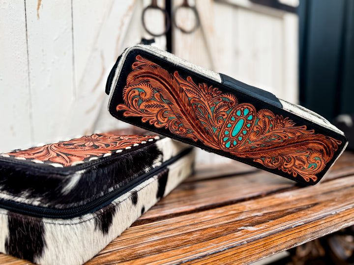 Tooled leather western hair tool travel cases displayed on rustic wood bench.