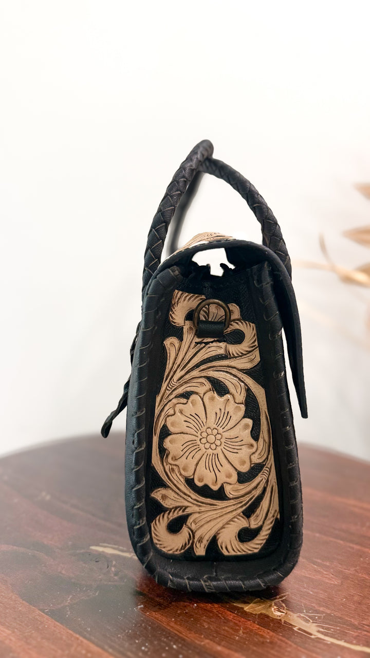 Side profile of black leather Western purse with floral tooled leather panel, braided trim and detachable shoulder strap hardware.