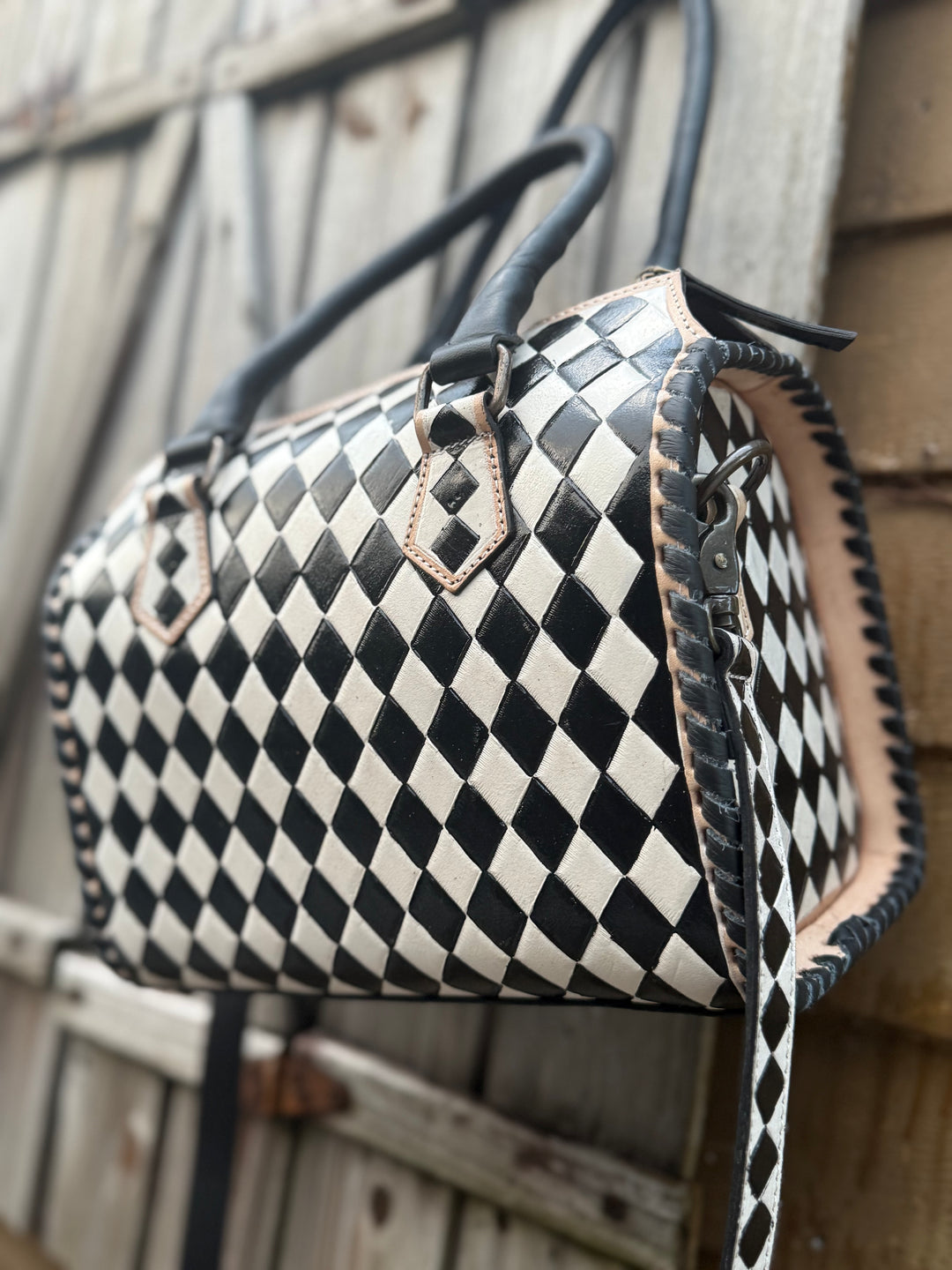 Side view of hand-tooled black and white checkered leather satchel with whipstitch edges.
