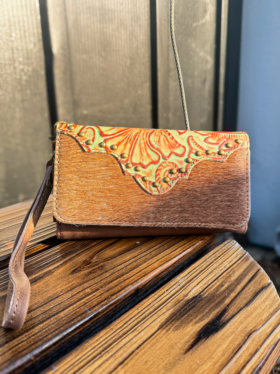 Brown cowhide leather phone wallet with green floral embossed leather pattern on a wooden surface