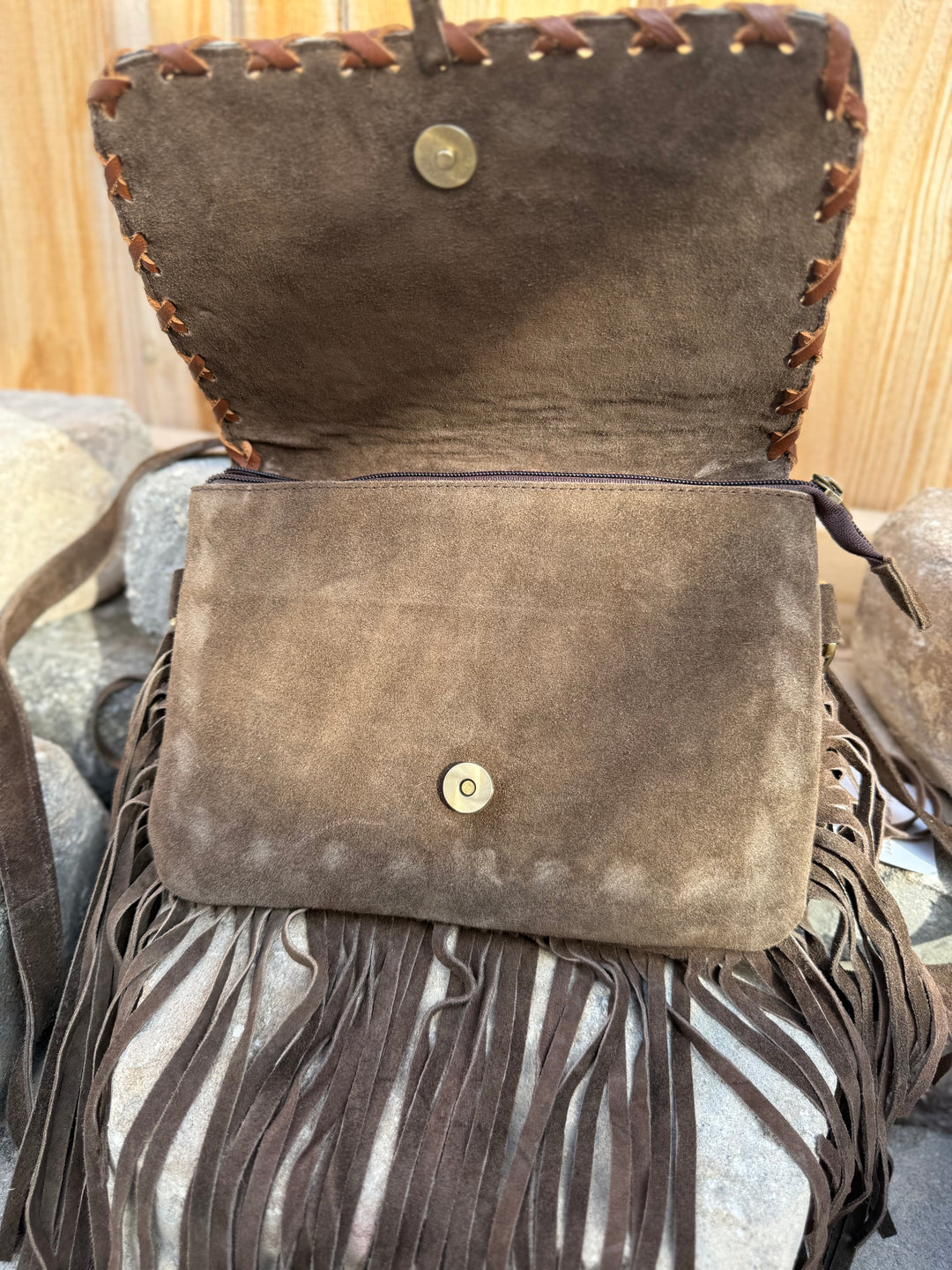 Brown suede handbag with fringes on a textured surface