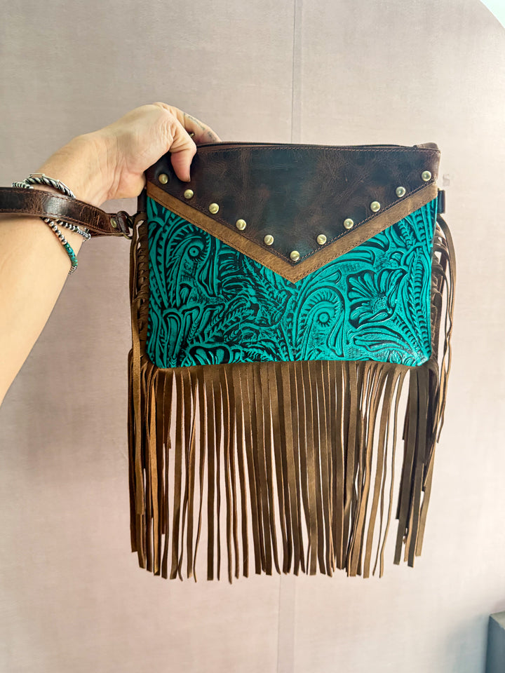 Handbag with turquoise pattern and brown fringe held by a person against a neutral background showing it can also be used as a clutch with the clutch leather hand strap