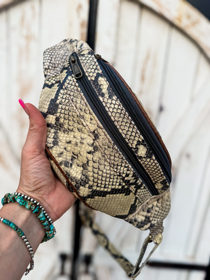 Hand holding a Butter yellow snake print genuine leather belt bag with adjustable strap and zipper pockets.