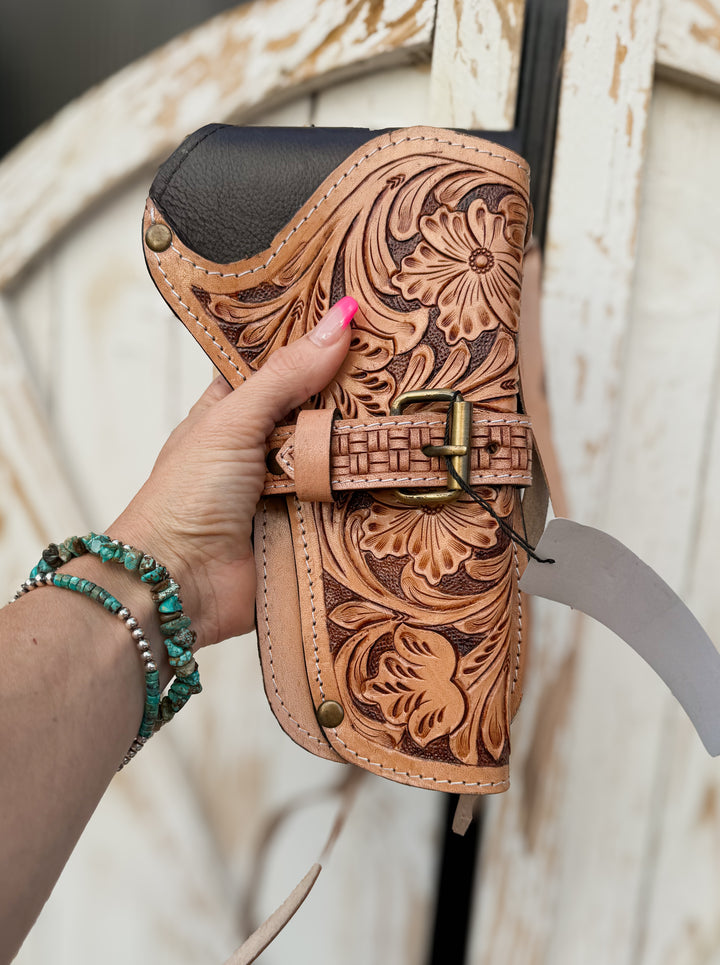 Handmade western revolver holster with floral tooled leather, basketweave buckle detail, and leather tie straps for belt carry.