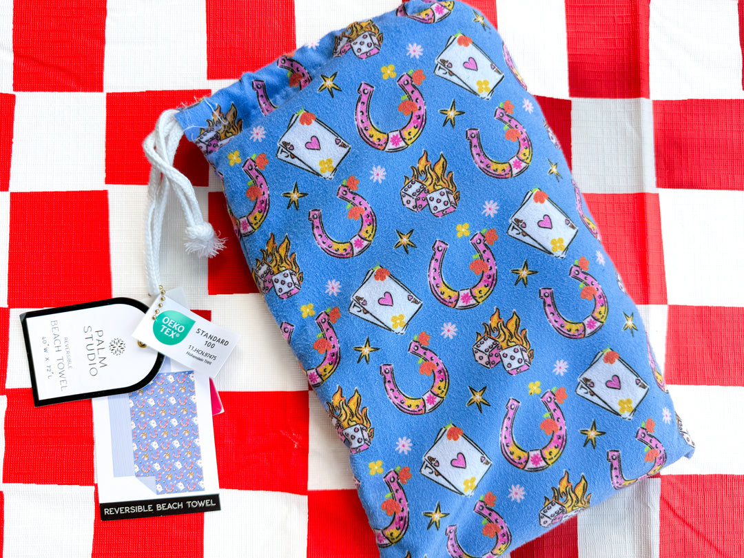 Blue reversible beach towel with western cowgirl print featuring horseshoes, dice, and lucky icons on a red and white checkered background.