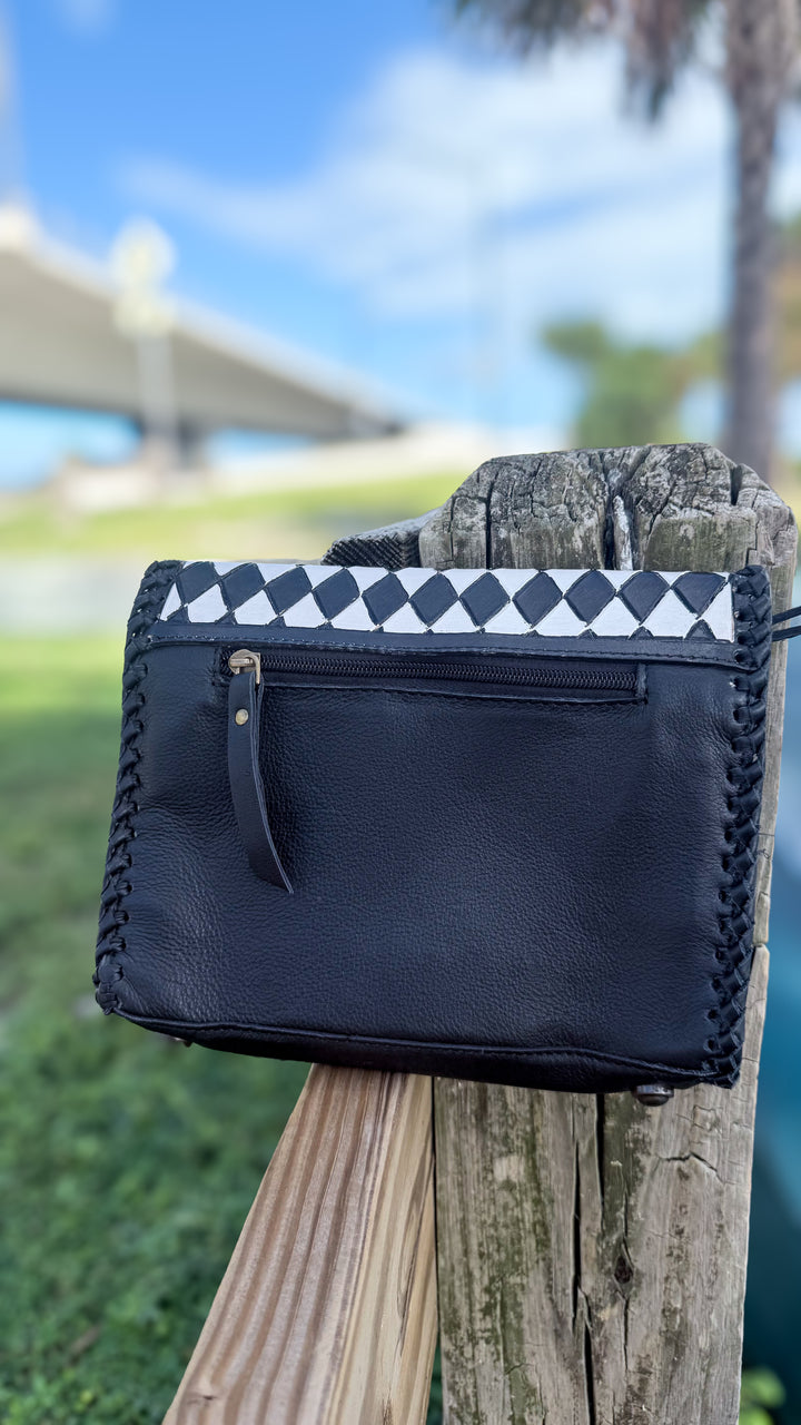 Back of black leather Western crossbody purse showing exterior zipper pocket, leather pull tab and diamond-check flap trim.