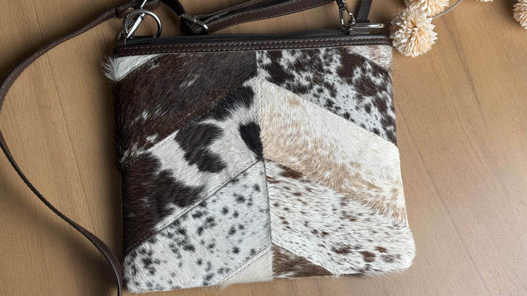 Brown and white genuine cowhide patchwork crossbody purse with adjustable leather strap, zip closure, and authentic hair-on hide panels.
