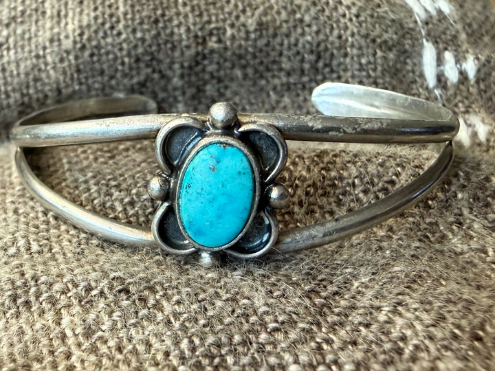 Native American Sterling Silver Childs cuff bracelet with a turquoise stone on a textured brown background