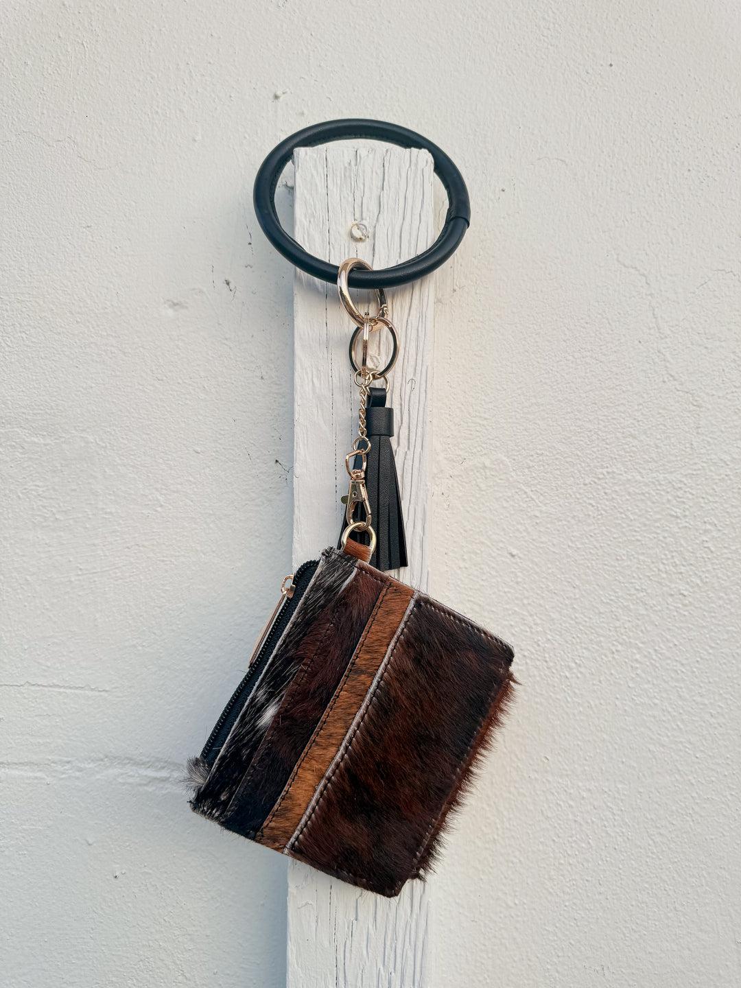 Dark cowhide wristlet wallet hanging from black bangle keyring with leather tassel.