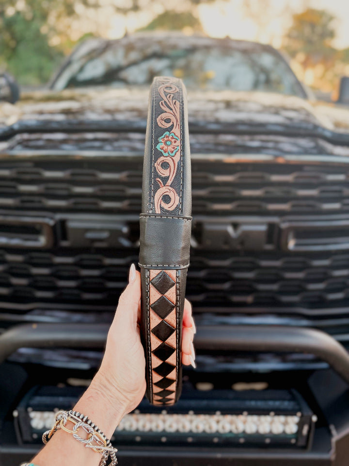 Hand holding a decorative western tooled leather steering wheel cover in front of a truck