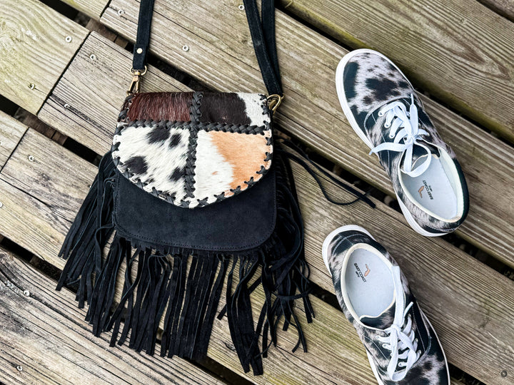 Black suede fringe crossbody bag with patchwork cowhide flap photographed with sneakers