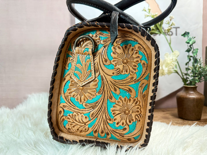 Close-up side view of floral tooled leather with turquoise painted accents and black whipstitched edge detailing on western speedy satchel handbag 