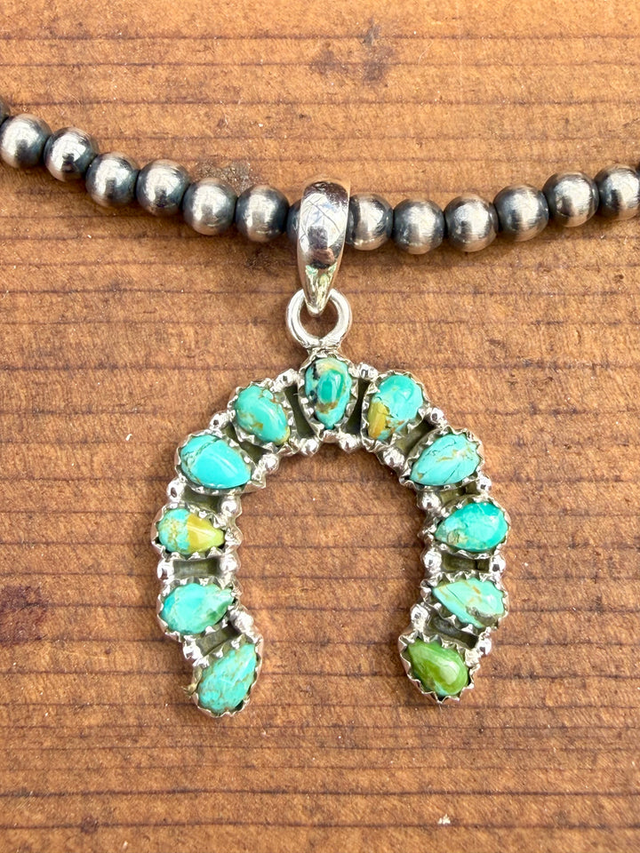 Sterling silver horseshoe pendant with green blue turquoise stones shown on Navajo pearl necklace
