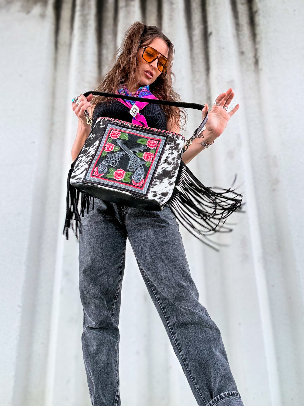 Woman carrying The Southern Draw by East Coast Carry, a black and white hair-on cowhide leather fringe bag with pink rose and Western artwork