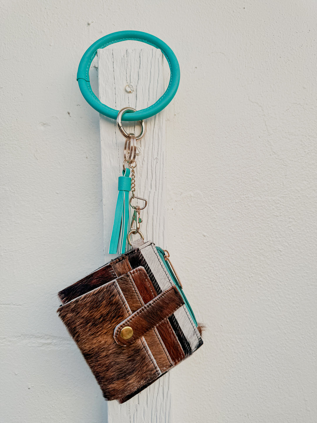 Cowhide wristlet wallet hanging from turquoise bangle keyring with tassel detail.