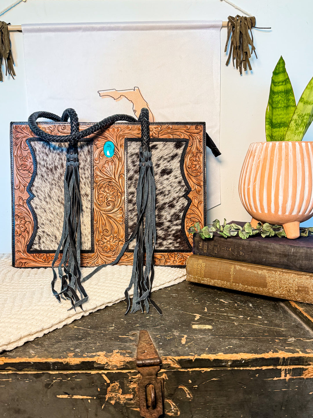 Brown tooled leather and black-and-white cowhide tote bag with turquoise stone detail and double back zippers.