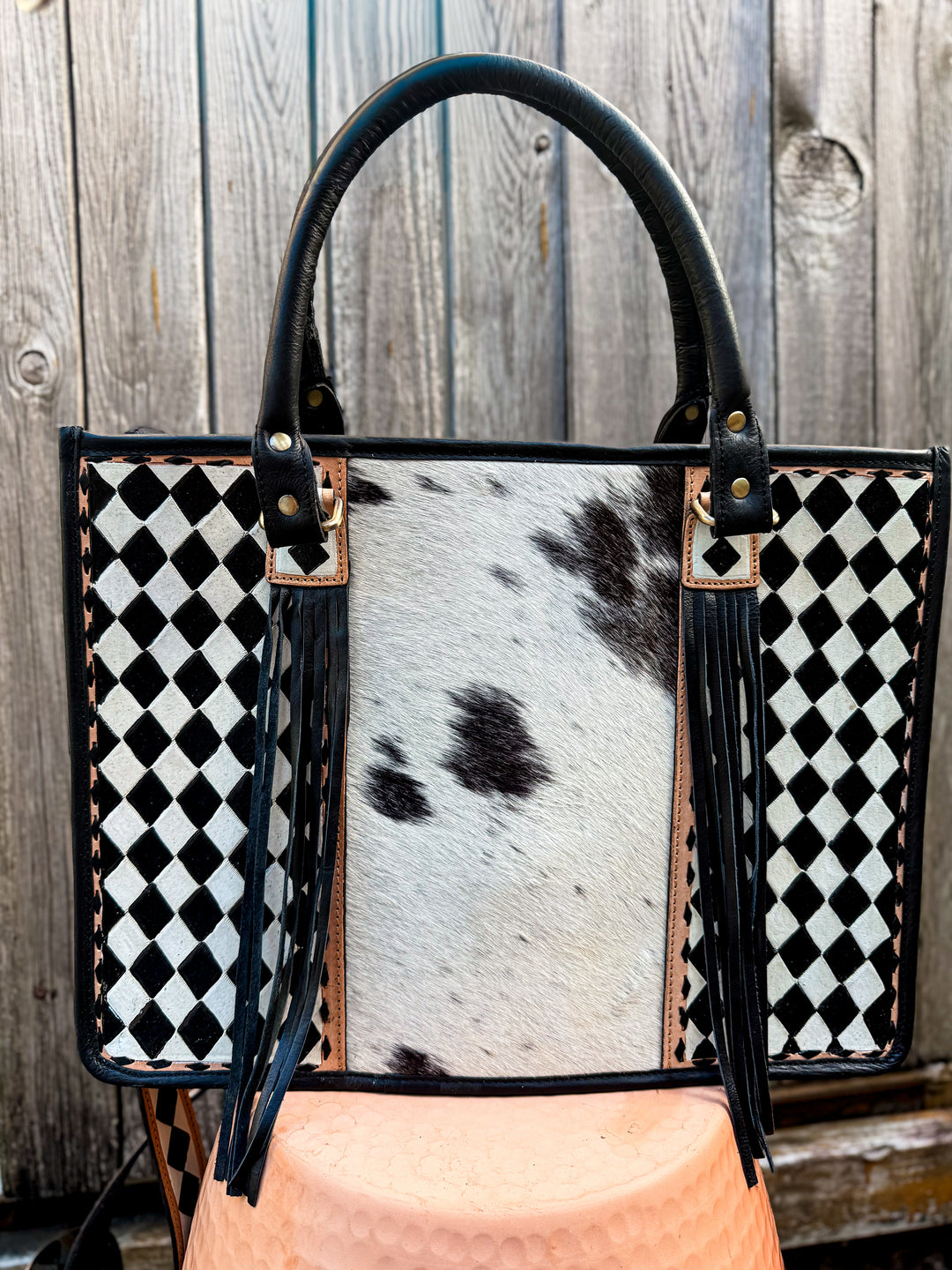 Handbag with black and white checkered pattern and cowhide leather back against a wooden background