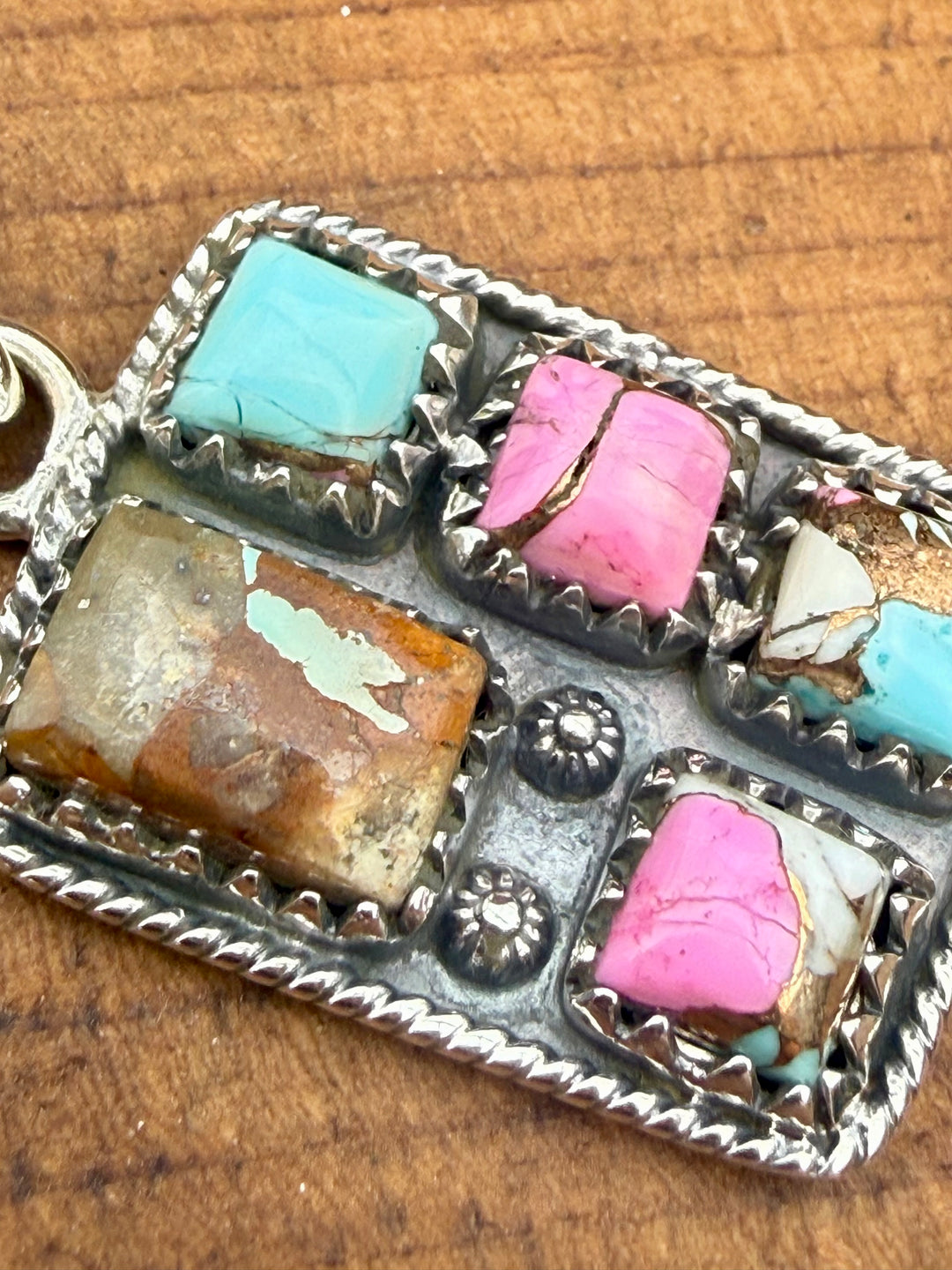 Close up of Sterling silver Mine #8 turquoise and pink composite southwestern pendant with stamped detailing and bale on wood background
