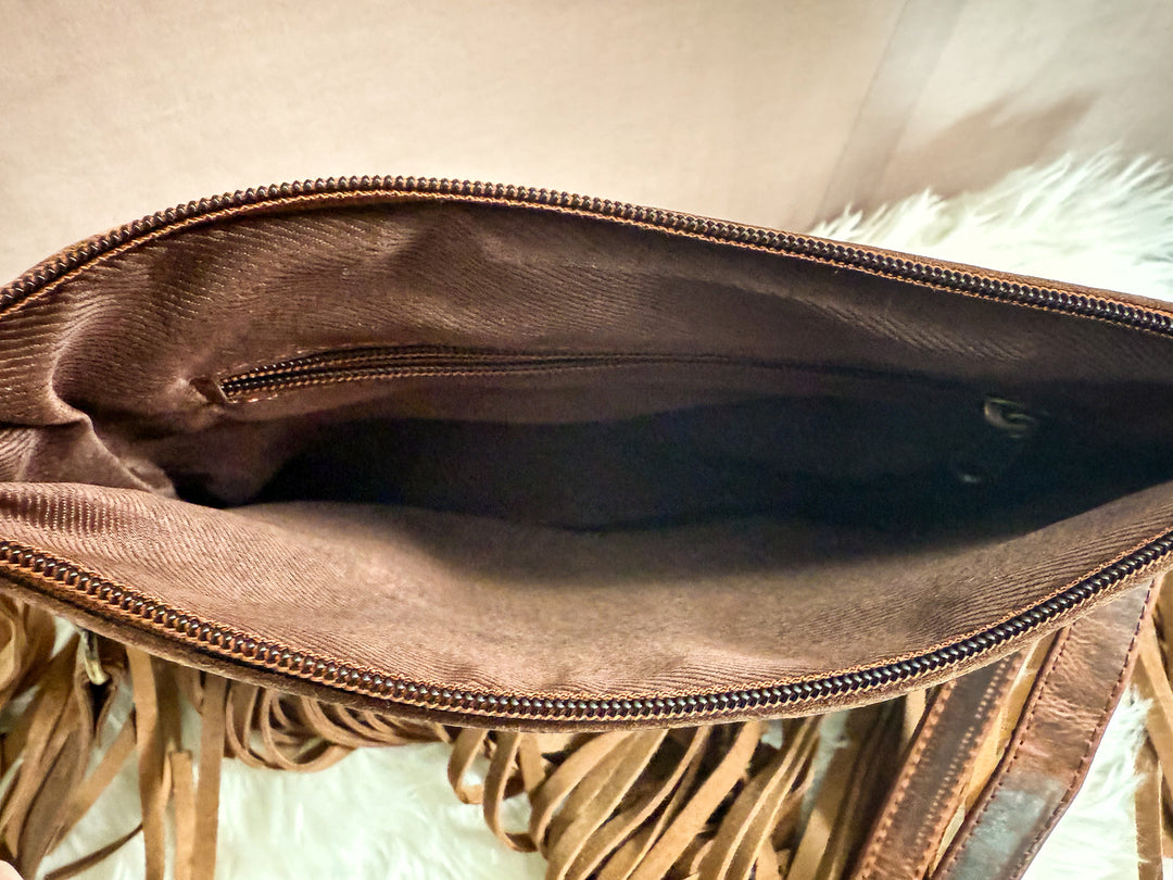 Brown leather clutch with fringe details on a neutral background