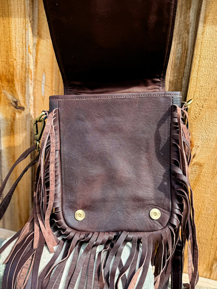 Inside flap of the Brown leather checkered bag with fringe details on a wooden surface