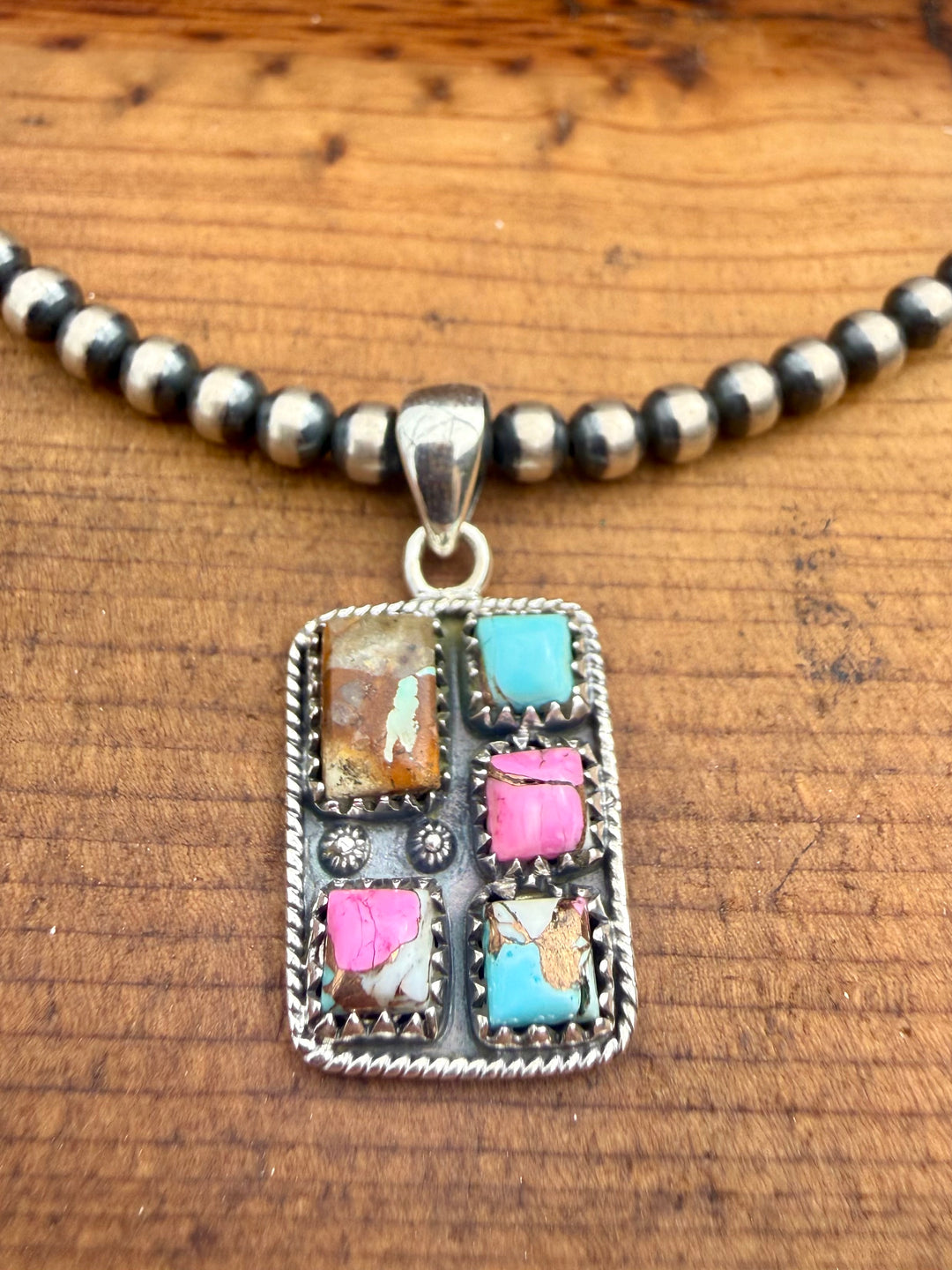Sterling silver Mine #8 turquoise and pink composite southwestern pendant with stamped detailing and bale on wood background
