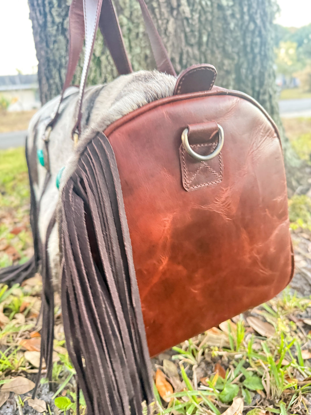 Brown full grain leather duffel bag with fringes on a grassy background
