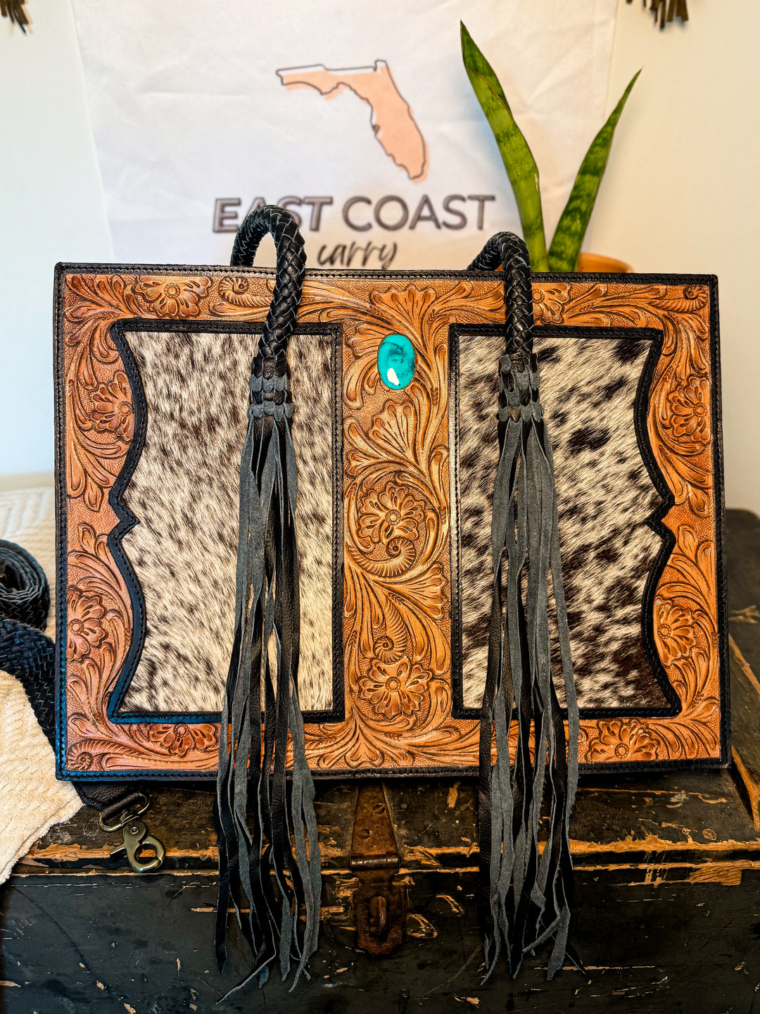 Tooled leather cowhide tote with turquoise concho and dual back zipper concealed-carry pocket.