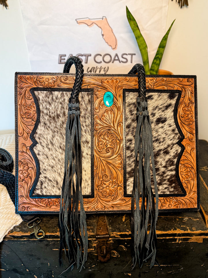 Tooled leather cowhide tote with turquoise concho and dual back zipper concealed-carry pocket.
