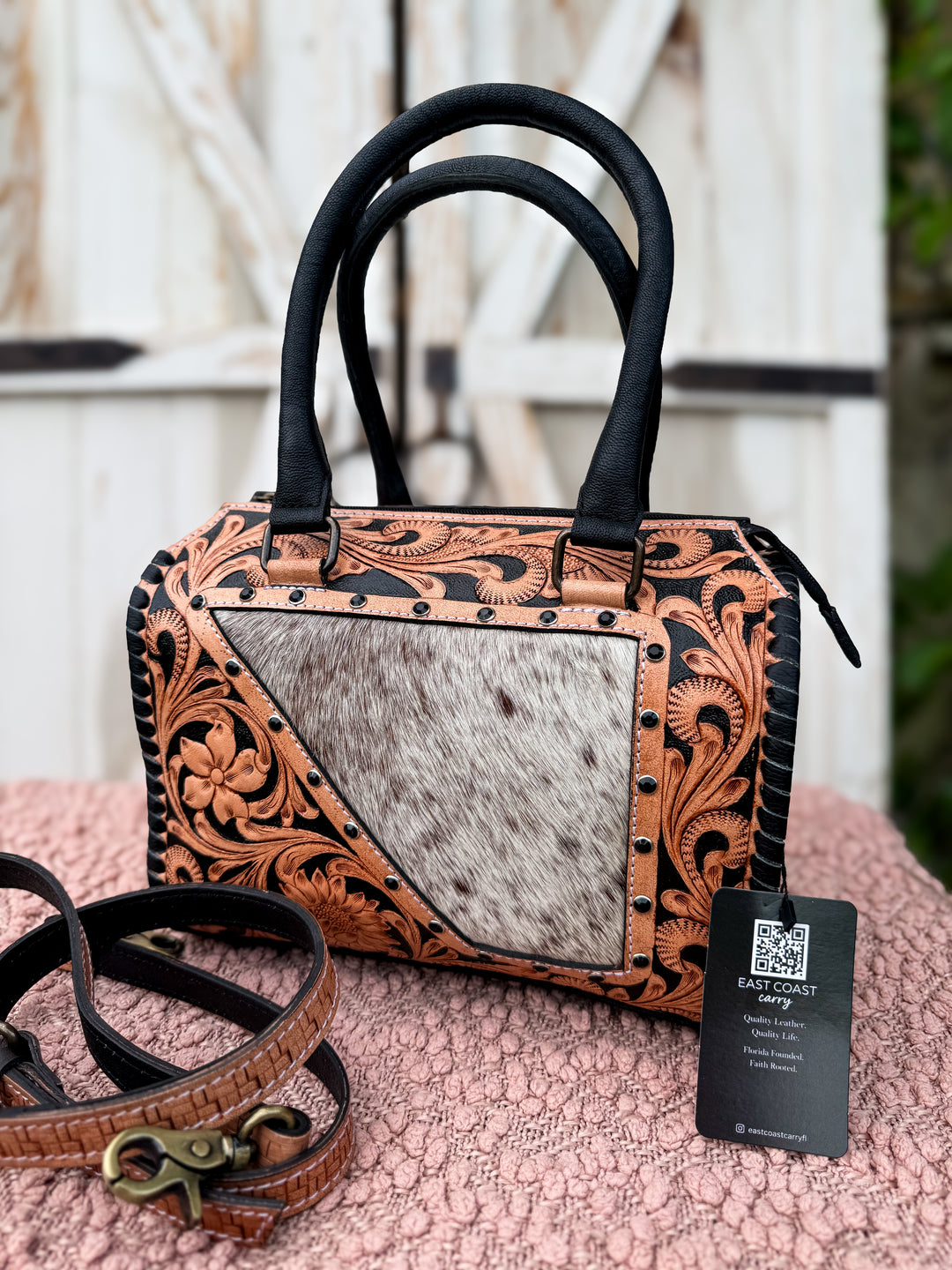 Western tooled leather speedy bag with cowhide panel and rhinestone studs. Medium structured handbag with crossbody strap and concealed carry space.