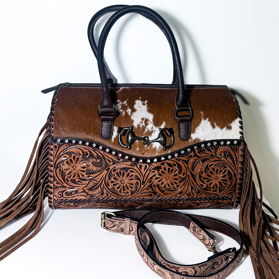 The Olde Money structured Western satchel with brown and white cowhide, floral tooled leather, horsebit accent, rhinestone studs and fringe.