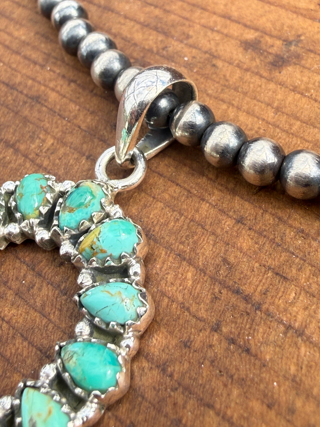 Sterling silver horseshoe pendant with green blue turquoise stones shown on Navajo pearl necklace
