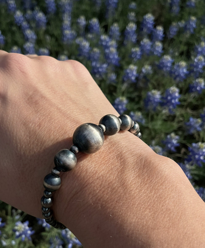 Graduated sterling silver bead stretch bracelet worn on wrist in natural light