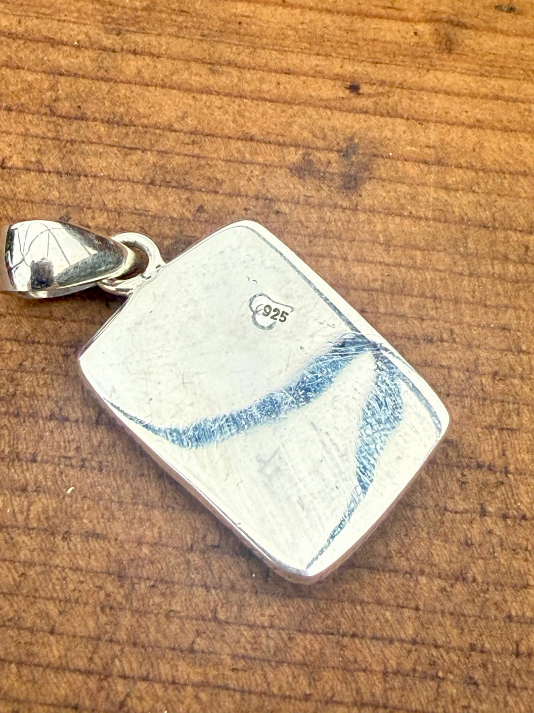 Back of Sterling silver Mine #8 turquoise and pink composite southwestern pendant with stamped detailing and bale on wood background showing 925 stamp 