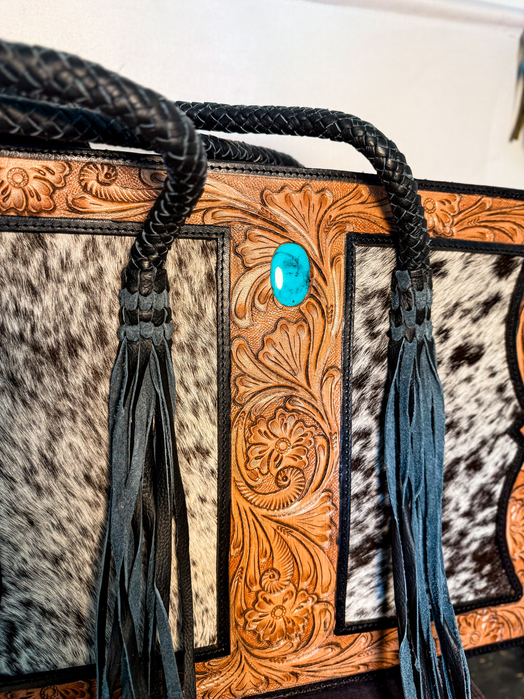 Western cowhide concealed-carry tote with hand-tooled leather front, turquoise accent, and dual zipper back pocket.