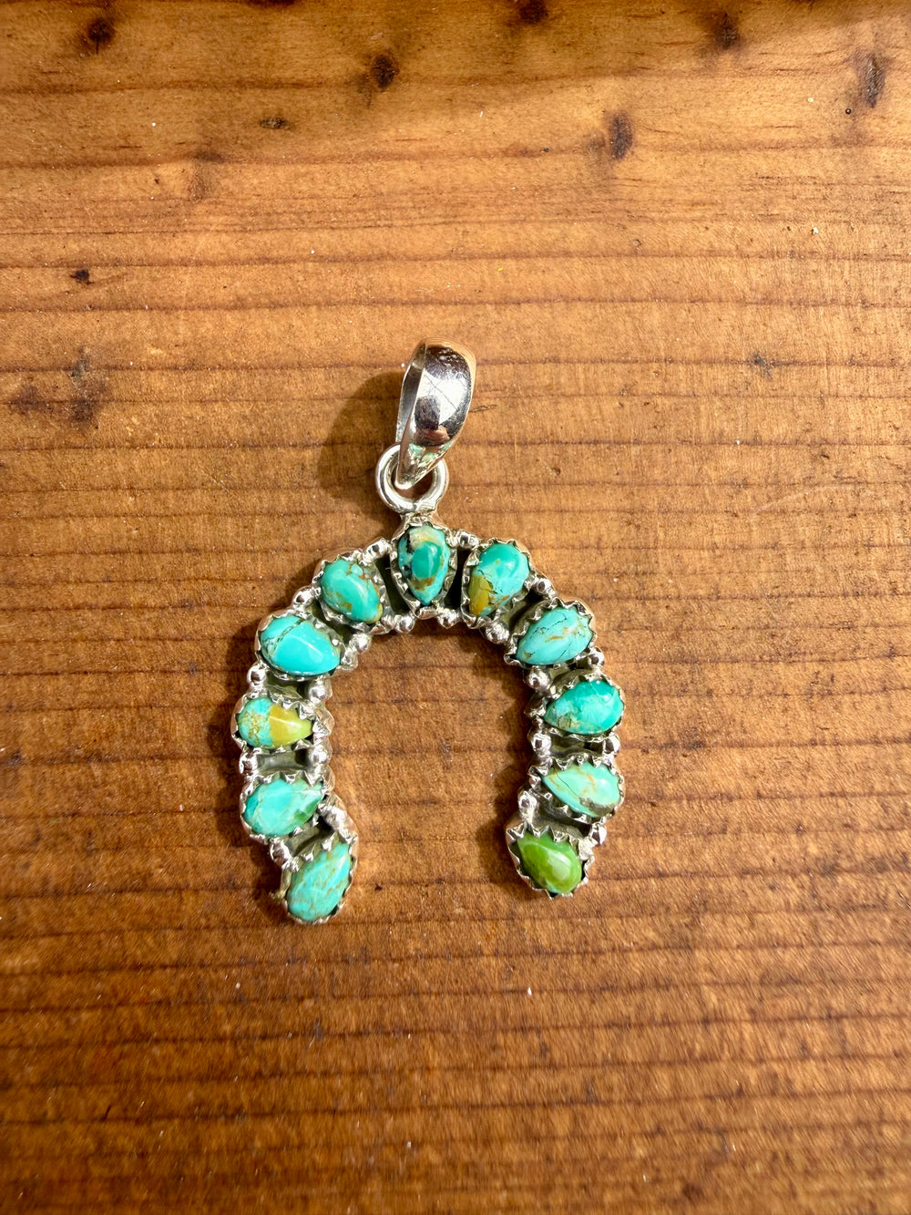 Sterling silver horseshoe pendant with green blue turquoise stones shown on wooden surface 